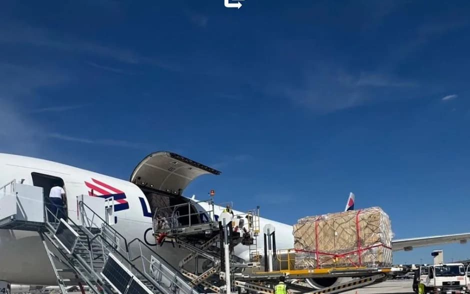 A freighter aircraft with its cargo door open and palletized cargo ready for loading, under a blue sky