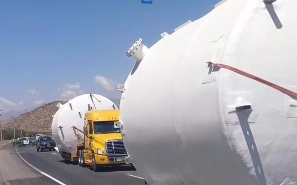 Two trucks carry the white oversized tanks along a highway in Chile